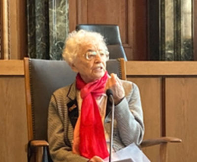 Ruth Weiss sitzt auf einem Stuhl und erzählt.